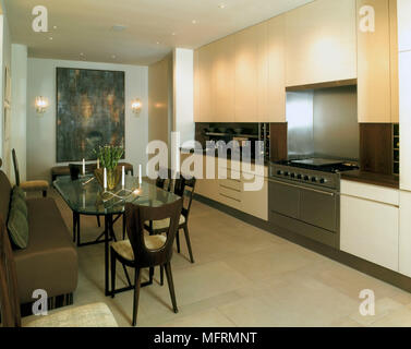 A modern open plan kitchen with dining area neutral units glass table chairs banquette seating tiled floor Stock Photo