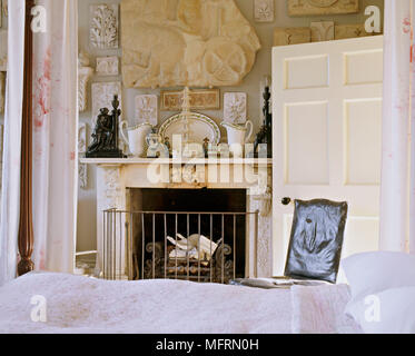 A detail of a traditional bedroom 18th century four poster bed fireplace with a display of plaster artifacts on the wall Stock Photo