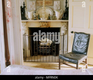 A detail of a traditional bedroom 18th century four poster bed fireplace with wrought iron fireguard leather chair Stock Photo