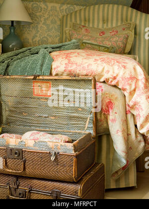 Old fashioned suitcases at foot of bed with stripe pattern headboard Stock Photo