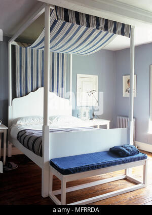 White wood four poster bed with blue stripe fabric canopy in modern bedroom Stock Photo