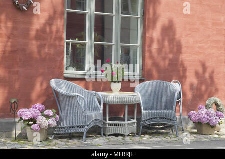 Two blue wicker chairs and a table and flowers by window Stock Photo