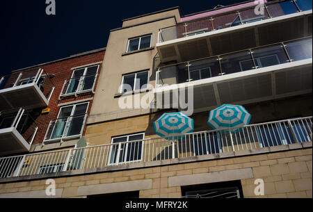 A beach front apartment building with two matching blue and white sun parasols on the balcony on a hot sunny day. Stock Photo