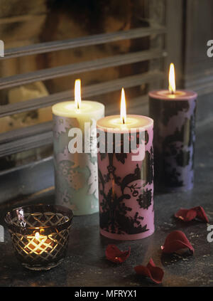 Three lit patterned candles with small tea light candle in glass on ledge Stock Photo