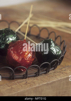Three toffee apples wrapped in red and green cellophane in a tray on old wooden bench top Stock Photo