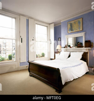 Traditional bedroom with double sleigh bed, white bed linens, and windows with shutters. Stock Photo