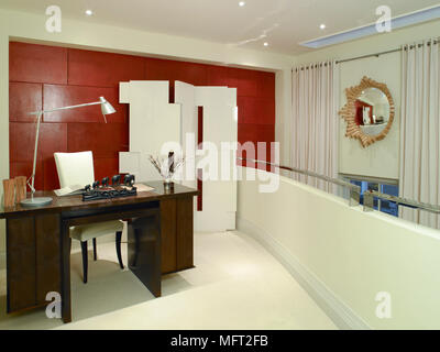 Modern home office loft with a red brick wall, wooden desk, and a sculptural folding screen. Stock Photo