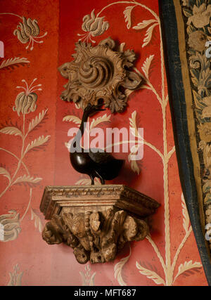 A detail of a traditional, red sitting room with gold pattern wallpaper, a gilt shelf with a ceramic bird figure Stock Photo