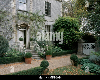 A detail of an exterior of a Georgian stone country house showing the front door entrance with steps and wrought iron railings, garden with low hedgin Stock Photo