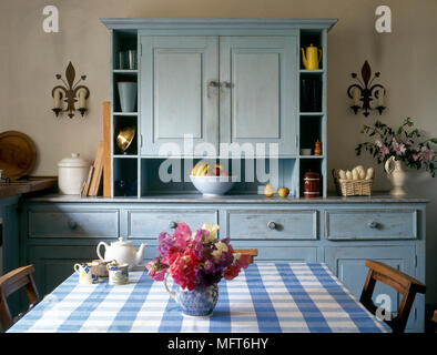 Country kitchen detail of a distressed, blue cupboard and a table with blue chequered tablecloth. Stock Photo