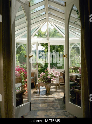 View through open french doors into a tiled conservatory with potted plants and a glass roof. Stock Photo