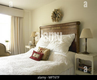 Neutral coloured bedroom with antique wooden headboard and white linen on bed Stock Photo