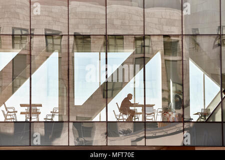 Denver, USA - November 04, 2016: An unidentified man sits by a table looking at his mobile phone in the glass passage of the Denver Art Museum. Stock Photo