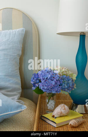 Blue hydrangea flowers and lamp on wicker table next to bed Stock Photo
