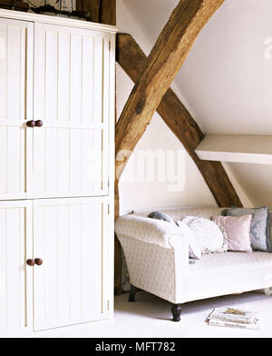 A detail of a country style sitting room with white walls beams built in cupboards cream sofa cushions Stock Photo
