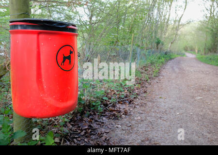 Dog waste (poo) bin painted bright red attached to a wooden post on a fence next to a path in the english countryside. Stock Photo