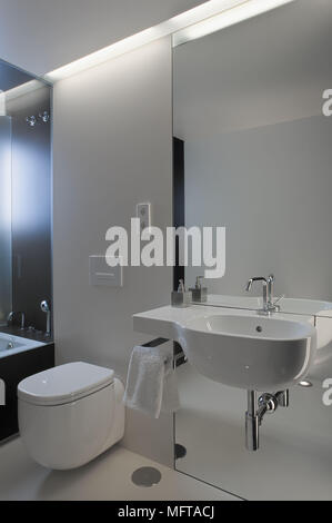 Wall mounted washbasin set on mirrored wall next to toilet with concealed cistern Stock Photo