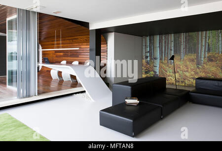 Black leather seating in modern open plan sitting room with view to wood panelled room Stock Photo