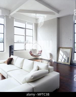Loft sitting room with sectional sofa, hanging seat, wood floor and sunny windows. Stock Photo