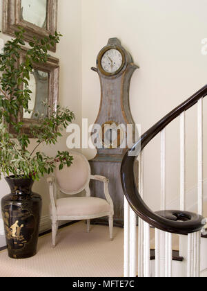 Period style chair in front of Gustavian style clock in hallway Stock Photo