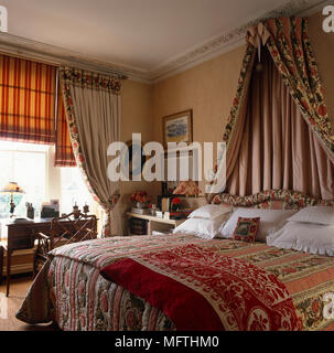 Double bed with fabric canopy above bed in terracotta bedroom with coordinating furnishings Stock Photo