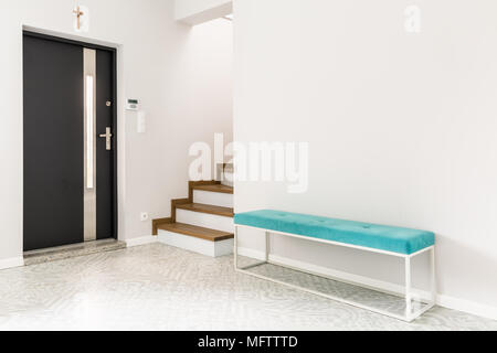 Black front door, stairs and a turquoise upholstered bench seat in a white entrance hall interior Stock Photo