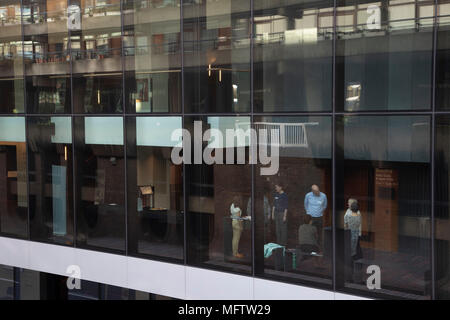 People talking inside modern glass building at Moorgate in the City of London, England, United Kingdom. As Londons financial district grows in height, the architecture has changed the face of Londons financial district, with many different companies occupying the various floors and levels. Stock Photo