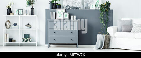 Simple posters, books and candles placed on grey cupboard standing in bright living room interior with white rack and decoration Stock Photo