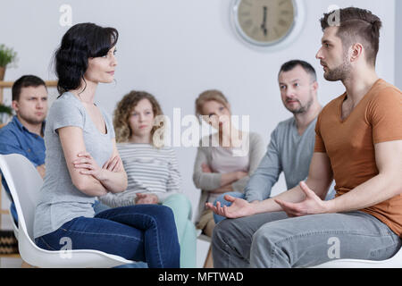 Couple talking about their relationship problems in front of other people during a marriage counseling session Stock Photo
