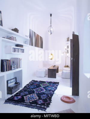 A modern white sitting room with fireplace retro light shade leather cushions bookshelves and Moroccan rug Stock Photo