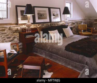 Bedroom with double bed and large throw.  Twin bedside lamps retro chair stained wooden floor with cow skin rug Stock Photo