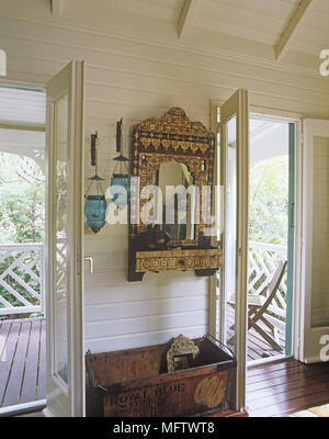 Details of an ornate gold decorative mirror in-between two exterior doors and above an antique wooden box. Stock Photo