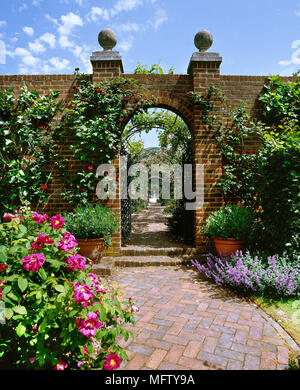 A detail of a walled garden with view through gate to a covered walk way, brick path, Stock Photo