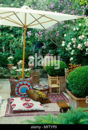 Cushions and chairs on rug beneath parasol in courtyard garden Stock Photo