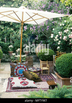 Cushions and chairs on rug beneath parasol in courtyard garden Stock Photo