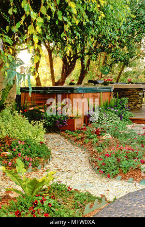 Hot tub with cover on in garden with planting of Helichrysum petiolare Limelight, Viola, Ficus, Asplenium nidus Stock Photo