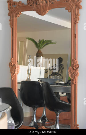 Details of a large framed mirror reflecting the view of a bohemian style dining room with black retro chairs and a large houseplant. Stock Photo