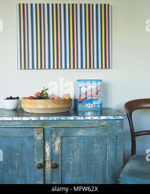 Details of a modern painting above a rustic cupboard with a bowl of fruit and an antique food tin. Stock Photo