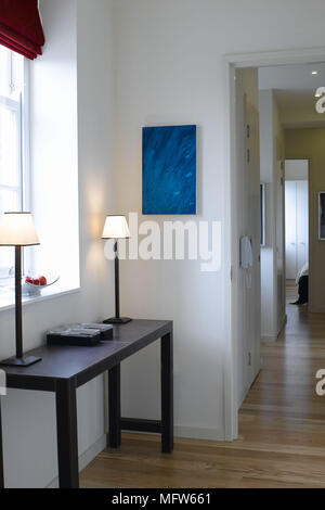 Matching lamps on a side table under a window in a modern hallway. Stock Photo