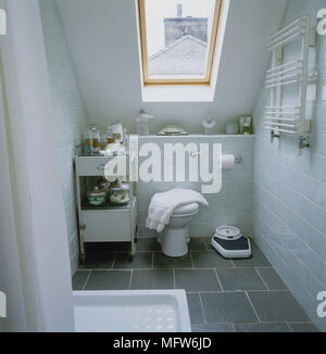 Modern attic bathroom with a slate floor subway tiled walls and a sloping ceiling with a skylight. Stock Photo