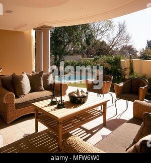 Tiled veranda with wicker seating arrangement, coffee table, and view of outdoor swimming pool and garden. Stock Photo