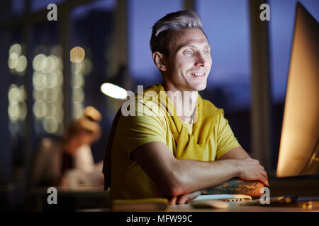 Young man working on computer at night in dark office. The designer works in the later time Stock Photo
