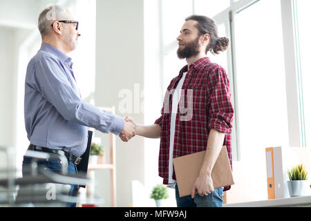 Two business partners shaking hands at office. They are greeting to each other Stock Photo