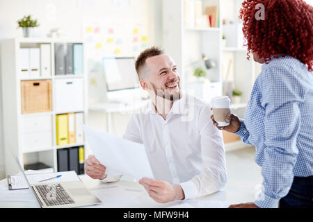 Business partners working together at office. They are laughing, drinking coffee and discussing documents Stock Photo