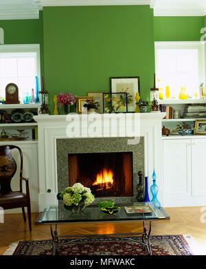 Glass topped coffee table in front of fireplace with lit fire in green sitting room Stock Photo