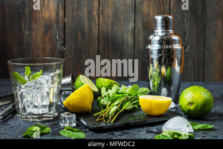 Mojito cocktail making. Mint, lime, glass, ice, ingredients and shaker on black stone background Stock Photo