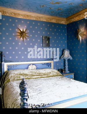 Blue bedroom with star motif wallpaper and painted bed with crushed velvet bedcover, Stock Photo
