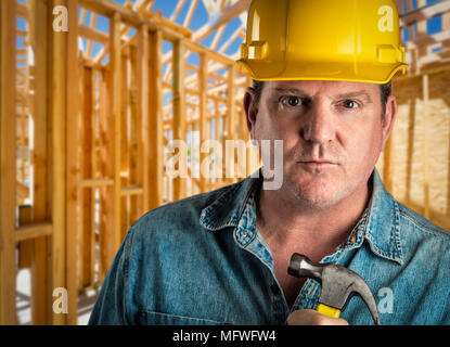 Serious Contractor in Hard Hat Holding Hammer At Construction Site. Stock Photo