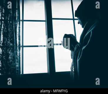 Mature man holding cup looking out of window: loneliness, mental health, living alone,...concept image Stock Photo