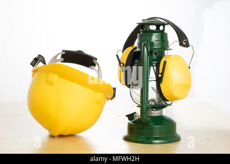 Protective helmet and oil lamp on a wooden table. Safety and health protection accessories for construction workers. White isolated background. Stock Photo